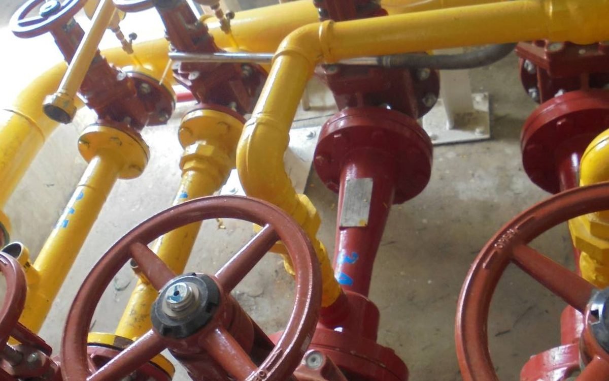 Red gate valves on yellow foam-line pipework — the wetted components cleaned or replaced during a foam system changeover